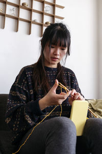 Woman knitting and filming through mobile phone at home