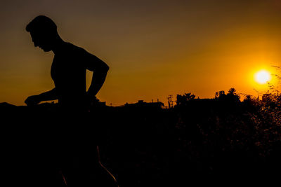 Silhouette man sitting against orange sky during sunset