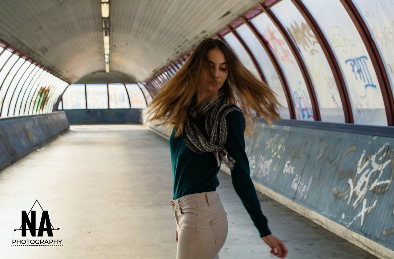 indoors, lifestyles, young adult, standing, casual clothing, young women, leisure activity, person, three quarter length, front view, long hair, full length, architecture, wall - building feature, looking at camera, portrait, built structure