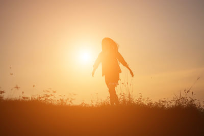 Silhouette woman standing on field against orange sky