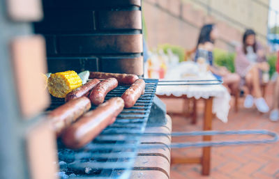 Close-up of sausages and corn on barbecue grill with friends sitting in background