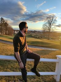 Side view of man standing on field against sky during sunset