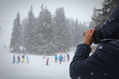 Cropped image of person photographing on snowcapped field during winter