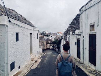 Rear view of mid adult woman with backpack standing on alley amidst buildings in city