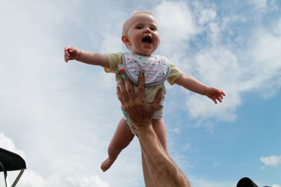 Low angle view of cute girl with arms raised against sky flying through the air 