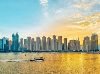 Sea by modern buildings against sky during sunset