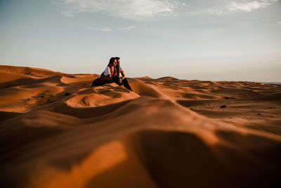 Woman on sand dune in desert against sky