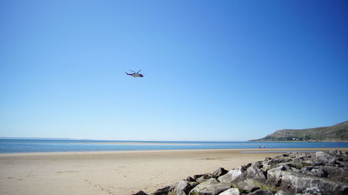 Low angle view of helicopter flying over sea against clear blue sky