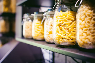 Close-up of raw pastas in jars on store shelves for sale