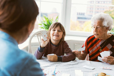 Happy boy playing cards with mother and great grandmother at home
