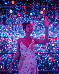 Woman gesturing while standing against illuminated lights at night