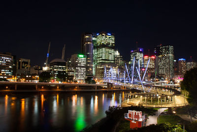 Illuminated buildings by river against sky at night