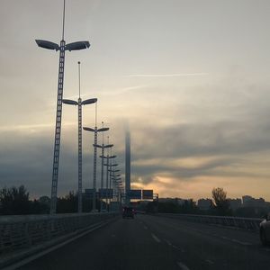 Street lights on road against sky during sunset