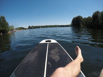 Person hand by lake against clear sky