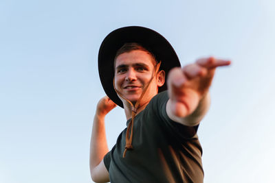 Young man smiling in cowboy hat showing flying hands against blue sky. male on blue sky background