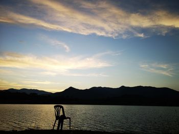 Silhouette man by lake against sky during sunset