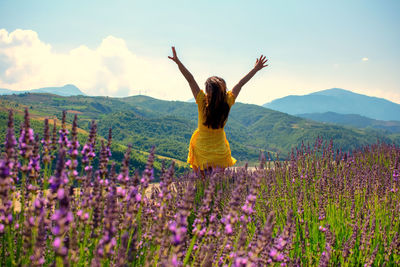 Rear view of woman with purple flowers on field against sky