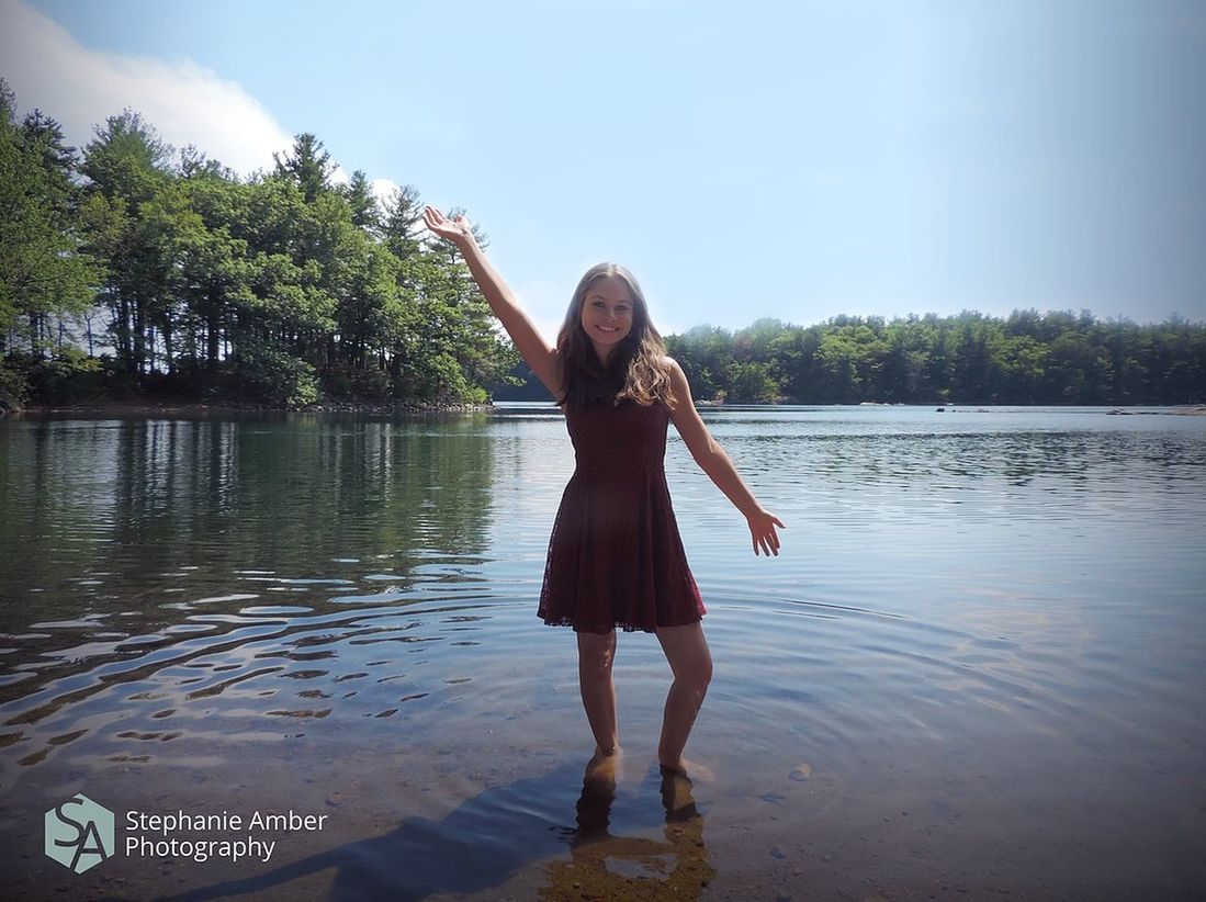 water, one person, lake, leisure activity, tree, young adult, real people, lifestyles, plant, full length, young women, sky, nature, smiling, women, looking at camera, standing, day, beauty in nature, fashion, human arm, outdoors, beautiful woman, hairstyle, arms raised