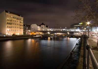 Illuminated bridge over river in city against sky at night