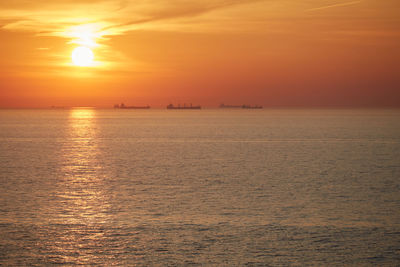 Commercial ships anchored at sea at sunset.