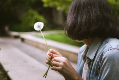 Close-up of woman holding dandelion while sitting in park