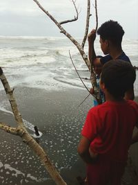 Brothers standing by bare tree at beach