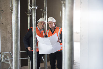 Two men with plan wearing safety vests in building under construction