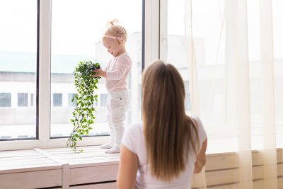 Rear view of mother looking at daughter by window