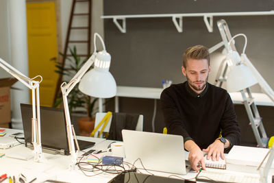 Confident young male professional working at illuminated desk in creative office