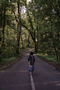 Rear view of woman walking on road amidst trees