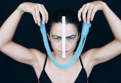 Portrait of young woman holding blue slimy against black background