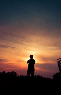 Rear view of silhouette man standing against orange sky
