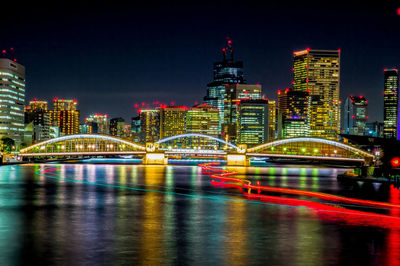 Illuminated buildings by river against sky at night