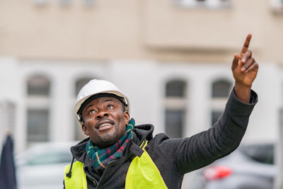 Thoughtful male engineer pointing while standing against building in city