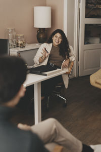 Businesswoman discussing with male coworker while sitting at desk in office