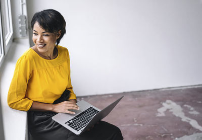 Smiling woman sitting at the window using laptop