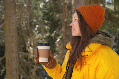 A girl drinks hot tea or coffee in a winter forest from a paper cup