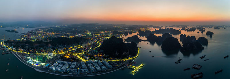 Aerial view of illuminated cityscape by sea against sky