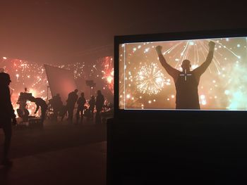 Silhouette people standing by illuminated lights against sky at night