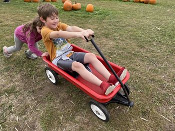 Boy playing with wagon on grass. sister pushing brother in a red wagon. pumpkin patch, kids