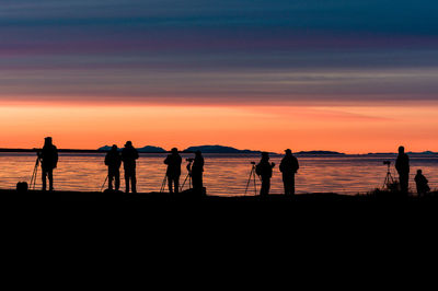 Silhouette people standing at beach during sunset