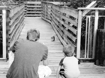 Rear view of father and son looking at squirrel on bridge