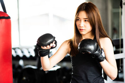Young woman punching bag while standing in gym