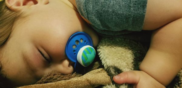 Close-up of baby boy with pacifier in mouth sleeping on bed at home