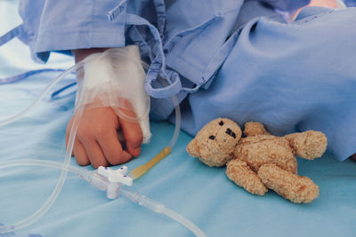 Cropped image of child sitting with teddy bear on bed in hospital