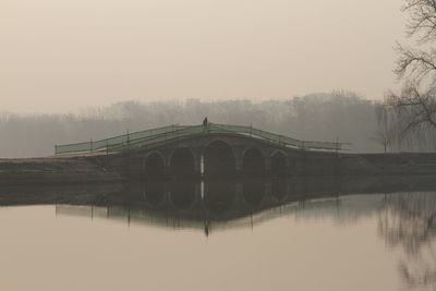 Bridge over river against sky during foggy weather