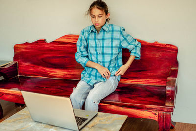 Pretty cute girl student sits on the sofa looking at the laptop on vacation alone inside the house.