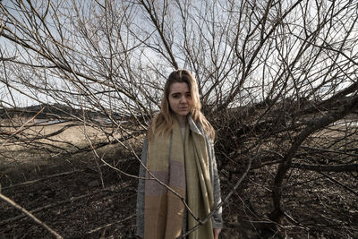 Portrait of young woman standing on bare tree