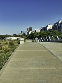 Road by buildings against clear blue sky