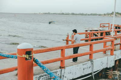 People on railing by sea against sky